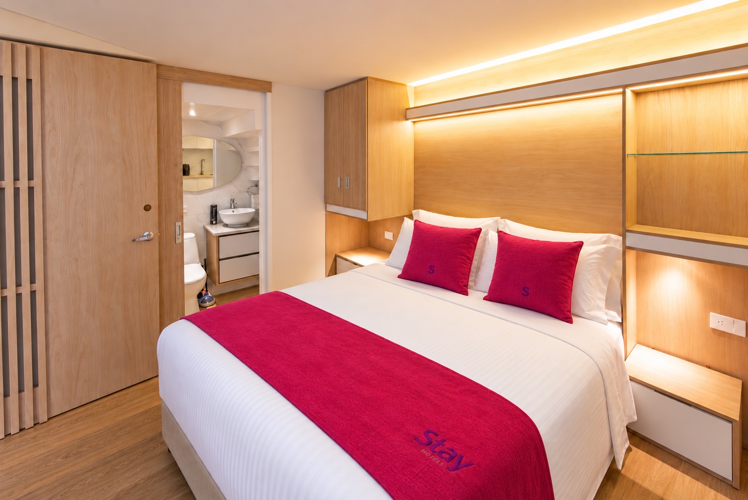 Habitación con identidad Stay: almohadas y pie de cama magenta, lencería blanca y acabados en madera